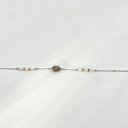 A delicate silver chain bracelet featuring a central oval cluster of small clear stones, flanked by white pearl-like beads and tiny gold spacer beads, laid flat on a white background.